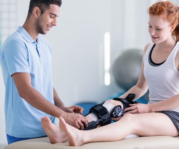 Smiling woman with stiffener on the leg and happy physiotherapist